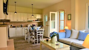 Une cuisine avec des meubles blancs, un coin repas avec une table et des chaises, et un salon avec un canapé et des coussins.