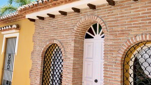 A building with a yellow facade, a brick lower section, and a tiled roof. There are two windows with decorative metal grilles and a white door. - CHALET WITH PISICINA AND VIEWS OF DREAM (Almuñécar)