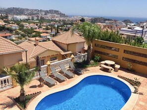 Ett bostadsområde med en swimmingpool, solstolar och utsikt över staden och havet.