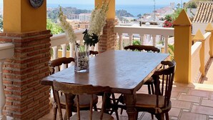 A covered patio with a table and chairs, a decorative light fixture, and a view of the sea. - CHALET WITH PISICINA AND VIEWS OF DREAM (Almuñécar)