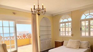 A bedroom with a bed, a chair, a chandelier, and large windows with views of the outside. - CHALET WITH PISICINA AND VIEWS OF DREAM (Almuñécar)
