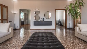 Een moderne woonkamer met een zwart voetenbankje, twee witte banken, een grote spiegel en een potplant.
