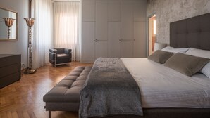Een slaapkamer met een groot bed, een stoel, een kledingkast en een vloerlamp.