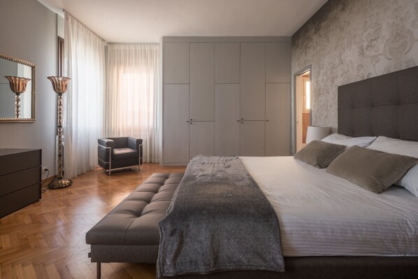 A bedroom with a large bed, a chair, a wardrobe, and a floor lamp.