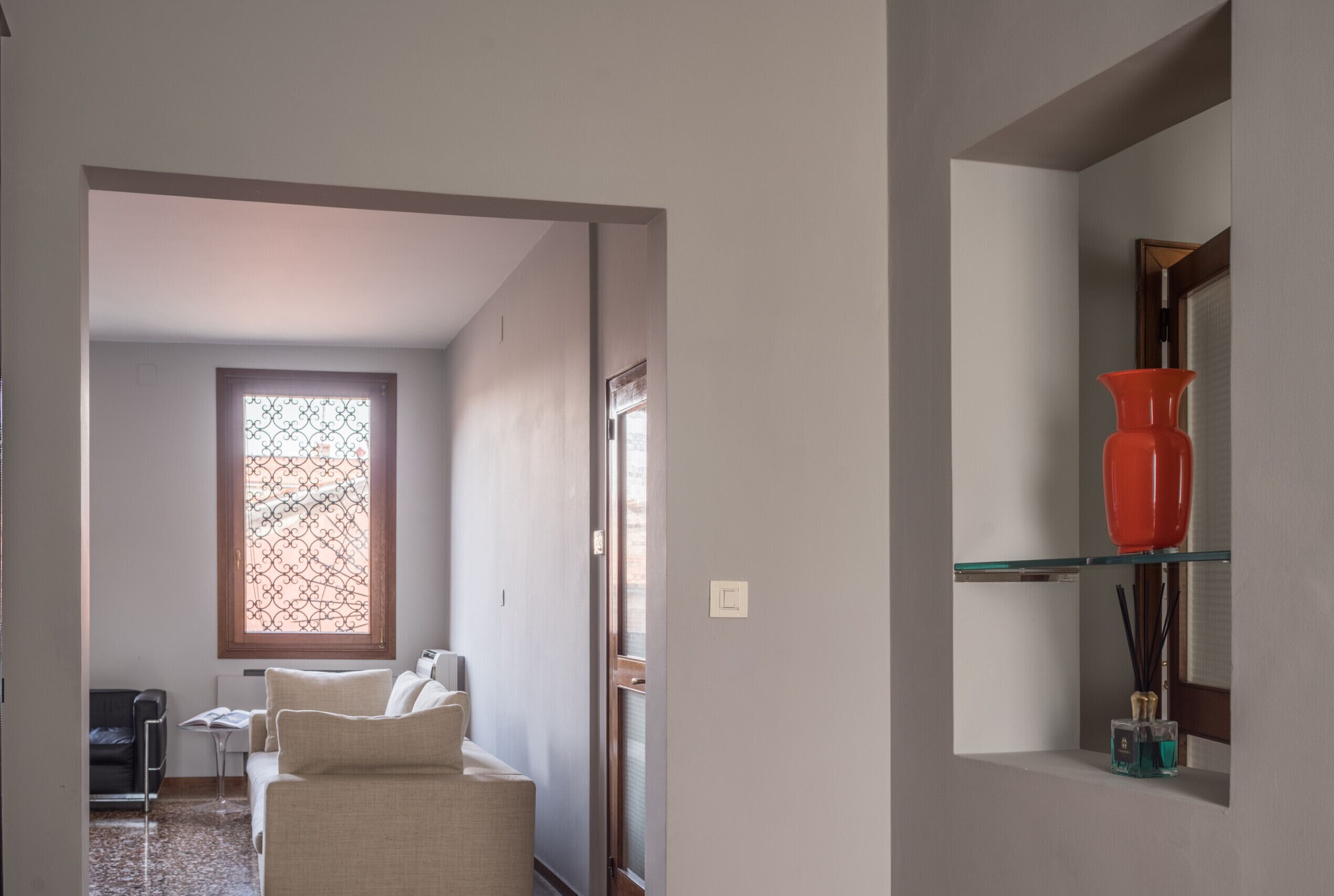 A hallway with a sofa, a table, and a window with a decorative screen.