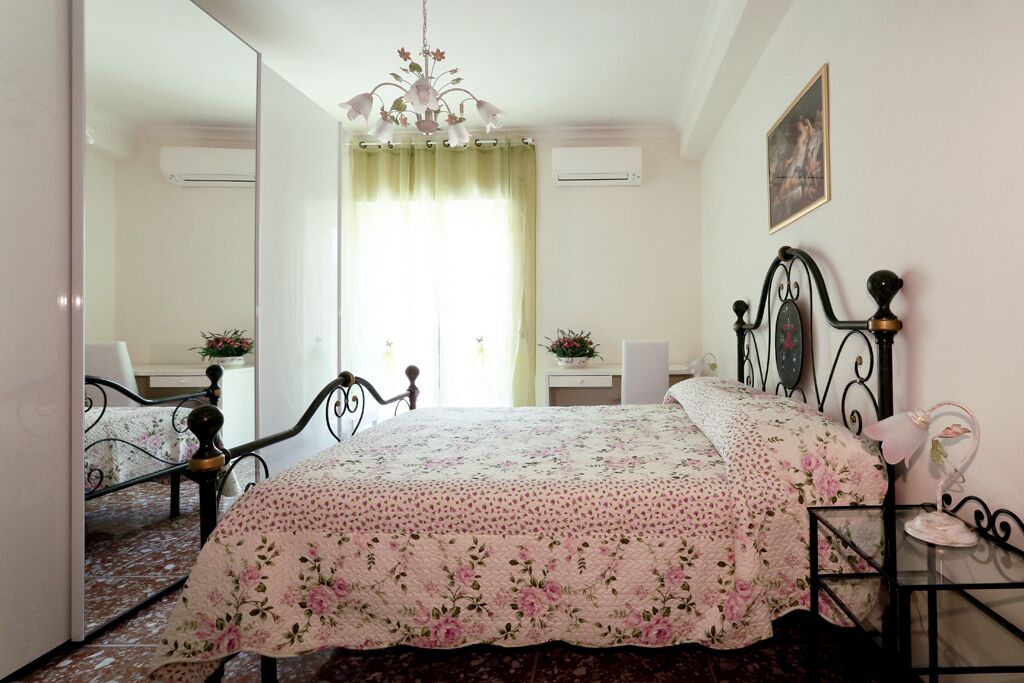 Een slaapkamer met een bed, een spiegel, een kroonluchter en een schilderij aan de muur.