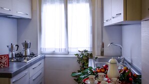 A compact kitchen with a gas stove, a kettle, and a sink. There is a window with sheer curtains, and a table with cups and a teapot. - LOVELY APARTMENT CENTER ROME 100M FROM VATICAN INTERNET FREE WI-FI (Roma)