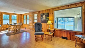 Interior de una cabaña de madera con comedor, un ventanal con vistas a un lago y un cartel en la pared.