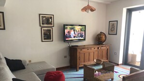 Una sala de estar con un sofá gris, un sillón de peluche rojo, muebles de mimbre, un televisor, cuadros enmarcados y un globo terráqueo sobre un mueble de madera.