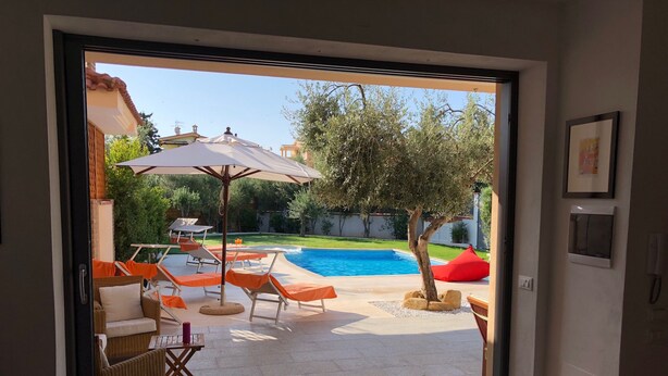 Puerta abierta a un patio con piscina, mobiliario exterior y un árbol.