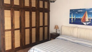 Un dormitorio con una cama grande, un armario de madera, un cuadro de veleros y una lámpara sobre una mesita de noche.