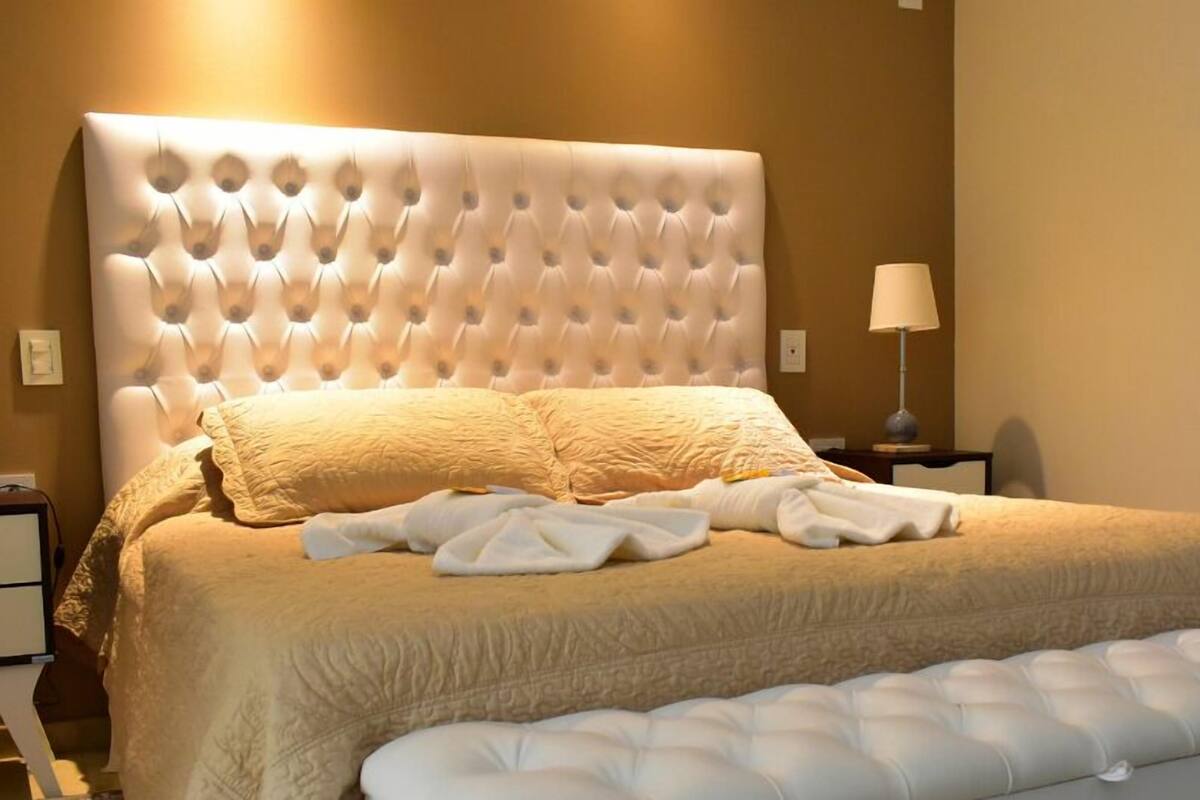 A neatly made bed with a tufted headboard, a bedside lamp, and a bedside table.