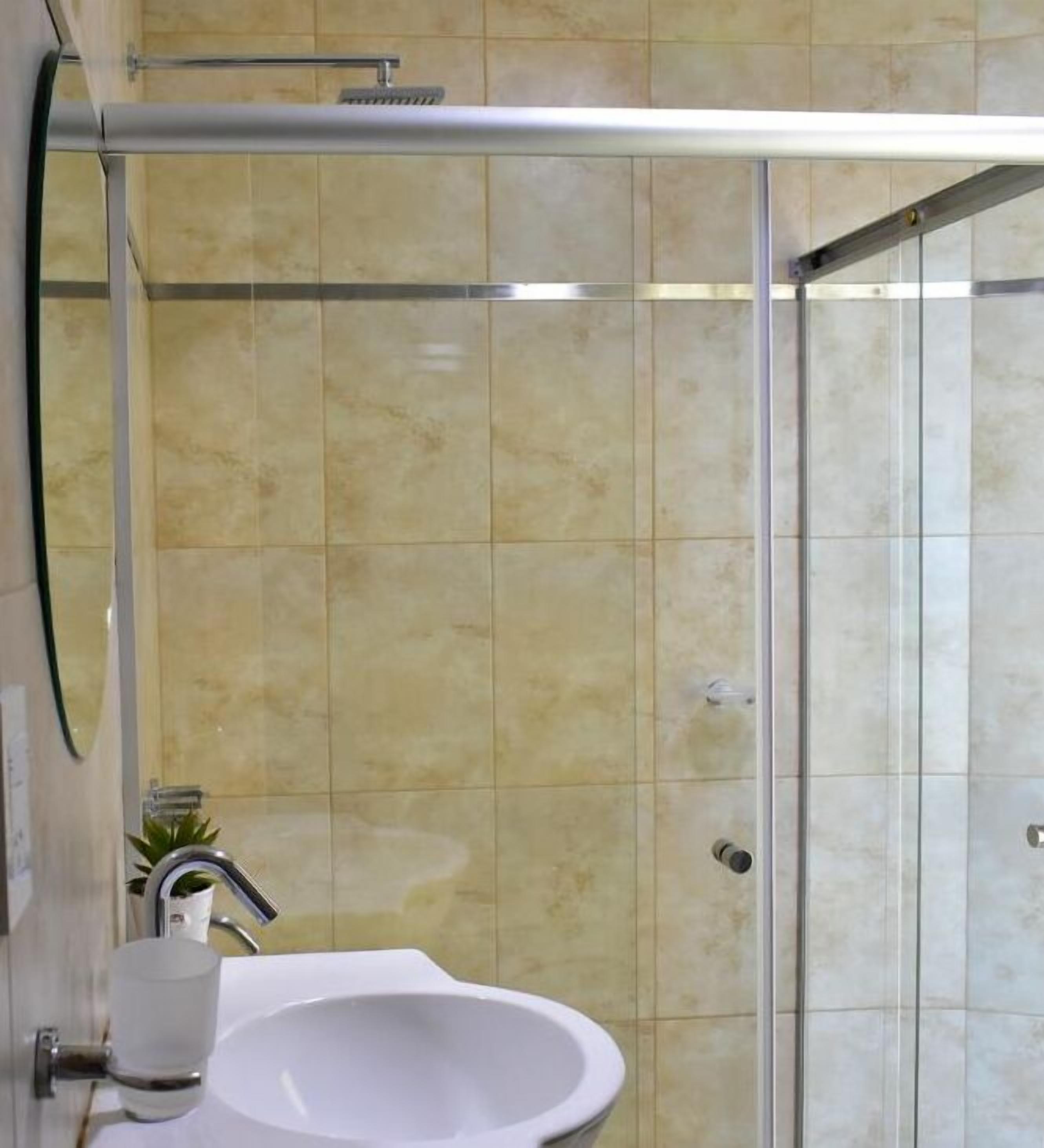 A bathroom with a white sink, a glass shower enclosure, and beige tiled walls.