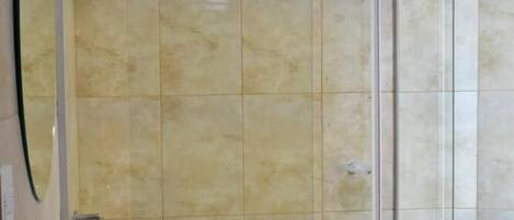 A bathroom with a white sink, a glass shower enclosure, and beige tiled walls.