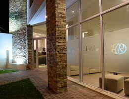 Exterior de un hotel moderno con pilares de piedra, entrada de vidrio y un logotipo en la pared de cristal.
