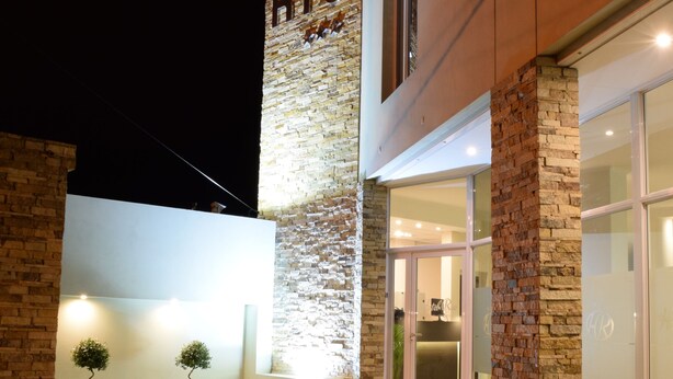 A hotel exterior with a stone facade, a well-lit entrance, and a paved area with small trees. - Hotel Rio (Chajarí)