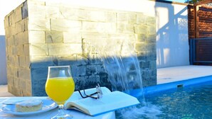 A poolside setting with a stone wall, a glass of orange juice, a plate with food, and an open book. - Hotel Rio (Chajarí)