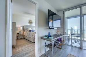 A hotel room with a bed, a TV mounted on the wall, a balcony with a view, and a small table with a lamp. - Bay Tree Bliss | Pool | Full Views of the Gulf! (Sarasota)