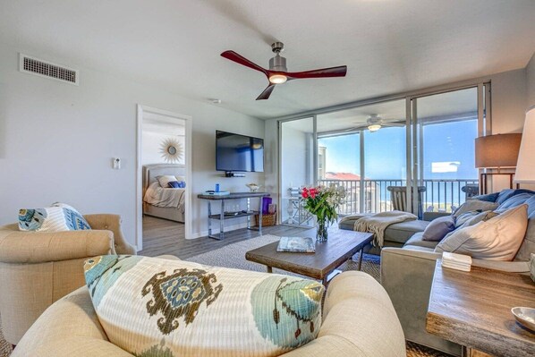A spacious living room with a ceiling fan, a television, and a balcony with a view.