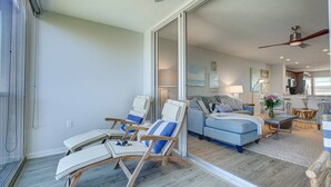 A spacious living area with a large sliding glass door leading to a balcony, a blue sofa set, and a wooden chair with a blue cushion. - Private Beach Access | Ocean Views | Pool | Full Views of the Gulf of Mexico | Bay Tree Bliss (Sarasota)