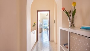 Un pasillo con suelo de baldosas, un arco, una zona de comedor al fondo y un jarrón con flores sobre una mesa.