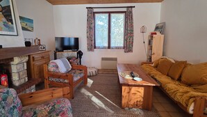 Ein gemütliches Wohnzimmer mit Holzbalkendecke, einem Fernseher, einem Sofa, einem Couchtisch und einem Kamin.