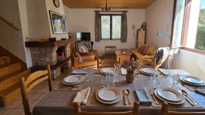 Ein Essbereich mit einem Holztisch, gedeckt für vier Personen, einem Kamin aus Stein und einem Fernseher im Hintergrund.