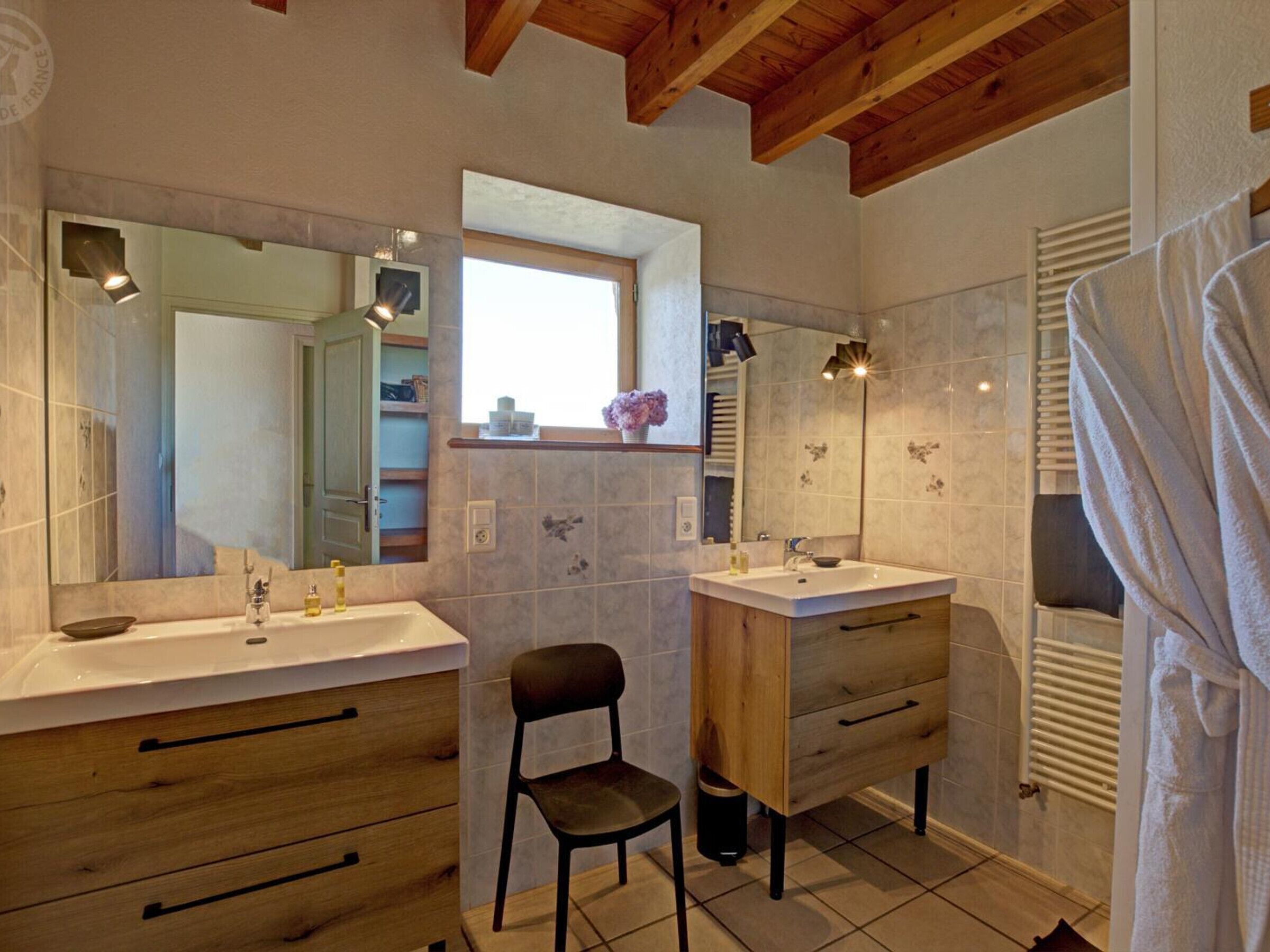 Une salle de bain avec deux lavabos, une chaise et une fenêtre.