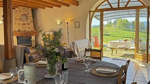 Un comedor con chimenea de piedra, una mesa dispuesta para una comida y vistas a un paisaje verde a través de un ventanal.