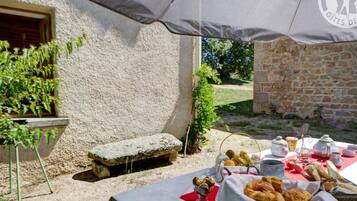 An outdoor dining setup with a table covered by a white tablecloth, a basket of croissants, and various breakfast items.
