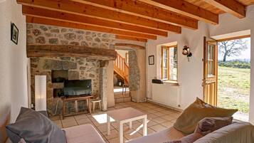 A cozy living room with a stone fireplace, wooden beams, a television, and a sofa.