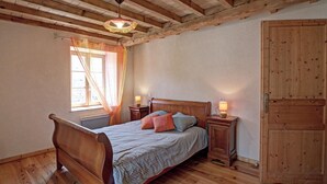 Quarto com cama de madeira, duas mesas de cabeceira com luminárias, janela com cortinas e guarda-roupa de madeira.