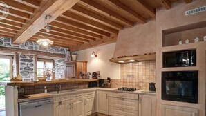 Cozinha com paredes de pedra, vigas de madeira e piso de azulejos.