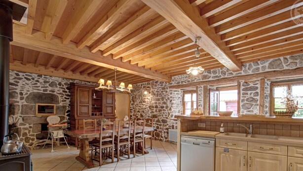 Uma cozinha rústica com paredes de pedra, vigas de madeira, uma mesa de jantar e um forno embutido.