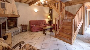 Uma sala de estar aconchegante com lareira, um sofá vermelho, escada de madeira e piso de azulejos.