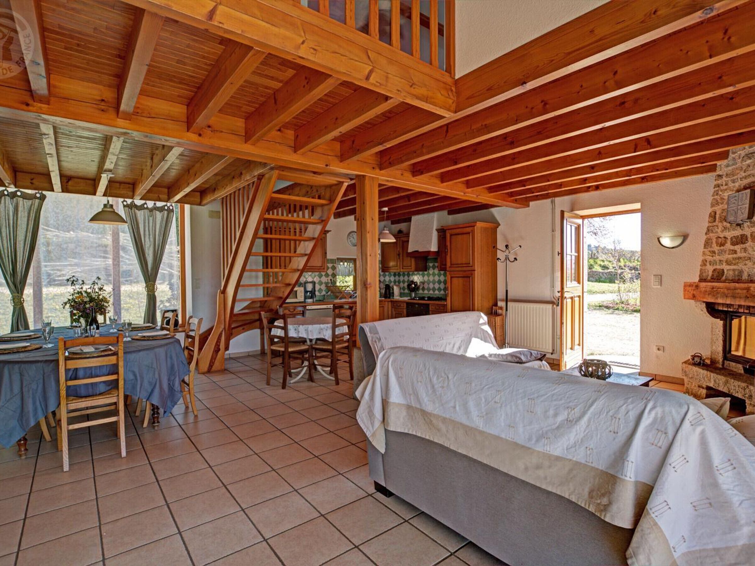 Een rustieke slaapkamer met houten plafond, een bed, een eettafel met stoelen en een trap.