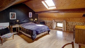A cozy attic bedroom with a sloped ceiling, a large bed, a stone wall, and a skylight.