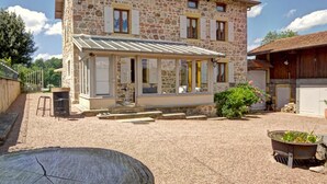 A stone house with a covered patio, a wooden barn, and a gravel driveway.