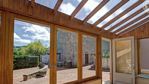 A sunlit room with wooden walls and a large glass door leading to an outdoor area with stone walls and a garden.