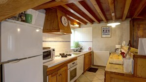 A kitchen with wooden cabinets, a microwave, a stove, and a clock on the wall. - Cozy cottage in natural park with pets allowed and modern comfort (Saint-Bonnet-le-Courreau)
