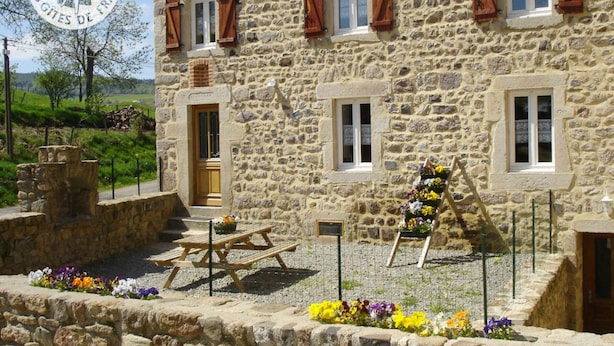A stone building with wooden shutters, a wooden bench, and flower arrangements. - Cozy cottage in natural park with pets allowed and modern comfort (Saint-Bonnet-le-Courreau)