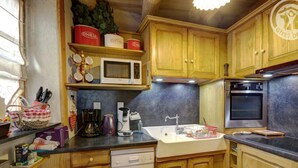 A kitchen with wooden cabinets, a microwave, a coffee maker, a toaster, and a dishwasher. - Charming Cottage with Garden in Estivareilles (Estivareilles)