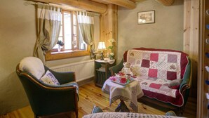 A cozy room with wooden beams, a green armchair, a red quilted sofa, a small table with a teapot, and a window with curtains. - Charming Cottage with Garden in Estivareilles (Estivareilles)