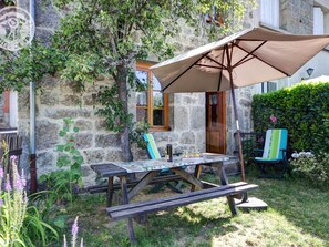 A rustic outdoor seating area with a wooden table and bench, a large umbrella, and a stone wall backdrop.