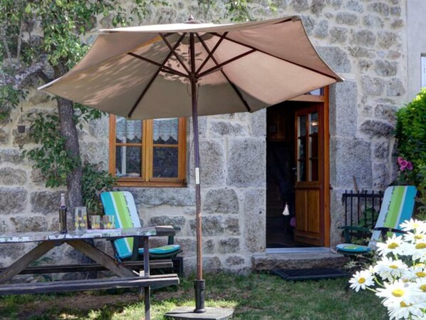 A stone building with a patio area featuring a table and chairs, an umbrella, and a door leading inside.