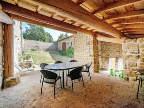 An outdoor patio with a stone wall, a wooden ceiling, and a table with chairs. - Charming 6-Person Cottage with Enclosed Garden in Montarcher (Montarcher)