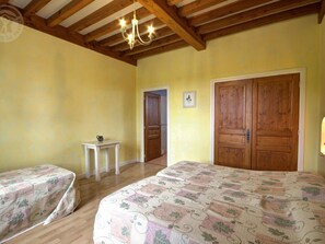 A room with two beds, wooden ceiling beams, a chandelier, and a door with a picture on the wall. - Spacious house with heated pool, 4 bedrooms in Chalain-le-Comtal (Chalain-le-Comtal)