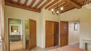 Een slaapkamer met houten deuren, een bed met een roze sprei, een kroonluchter en een badkamer zichtbaar door een geopende deur.