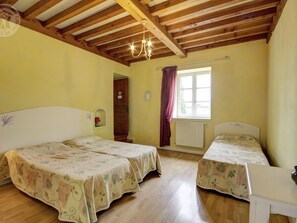 Een kamer met twee bedden, houten balken in het plafond, een raam met gordijnen en een radiator.