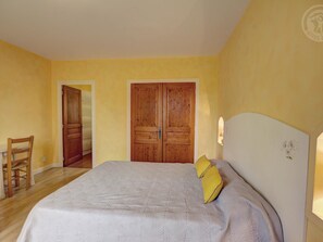 A bedroom with a bed, two wooden doors, a chair, and a nightstand.